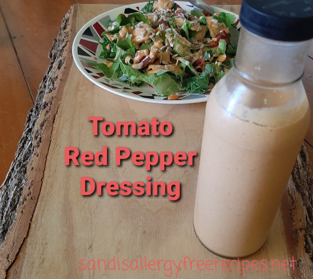 Plate of salad on a board with a bottle of salad dressing and red text saying Tomato Red Pepper Dressing sandisallergyfreerecipes.net